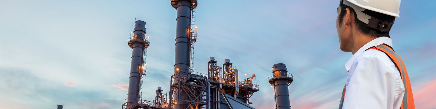 Engineer with notebook standing in front of oil refinery building structure in heavy petrochemical industry