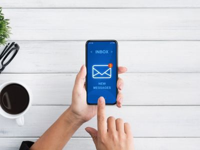 A persons hand holding a smartphone showing an email inbox.